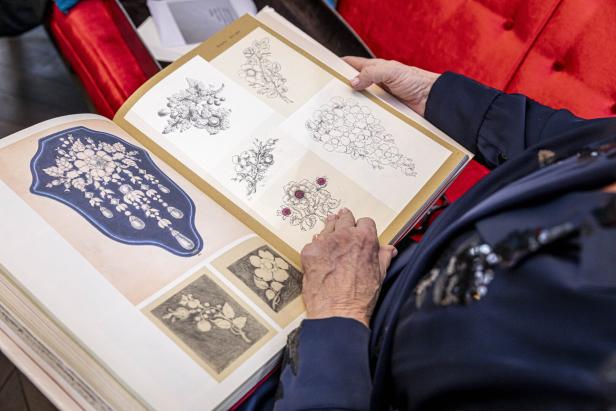 Eine Person blättert in einem Buch mit Illustrationen von Schmuckdesigns.