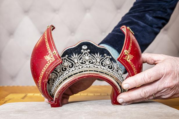 Eine Hand hält ein Diadem in einer roten, verzierten Schatulle.