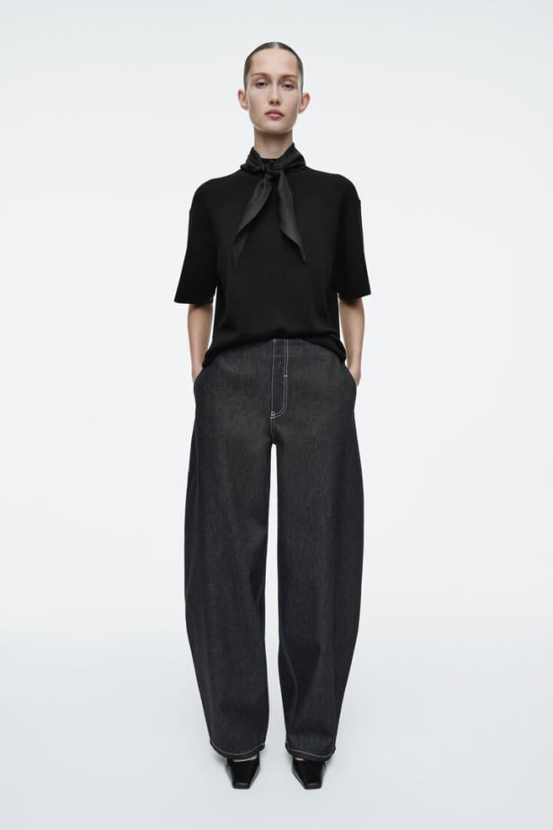 Eine Frau trägt ein schwarzes T-Shirt mit Schleife und weite Jeans.