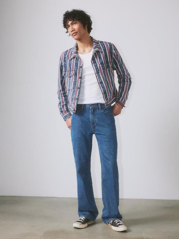 Ein junger Mann posiert in Jeans, T-Shirt und einer gestreiften Jacke.