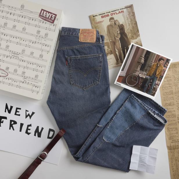 Eine Levi's Jeans liegt neben einer Bob Dylan Schallplatte und anderen Accessoires.