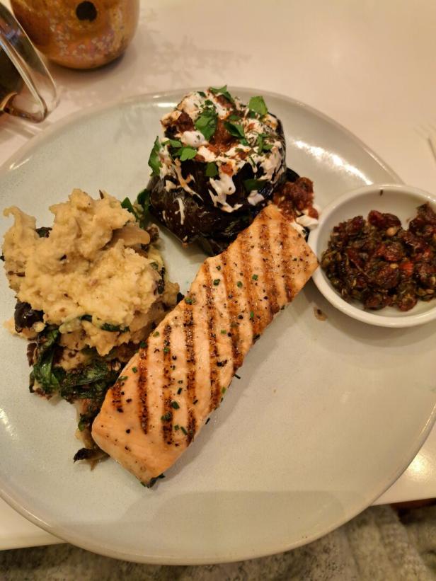 Ein Teller mit gegrilltem Lachs, gefüllter Aubergine und einem Dip.