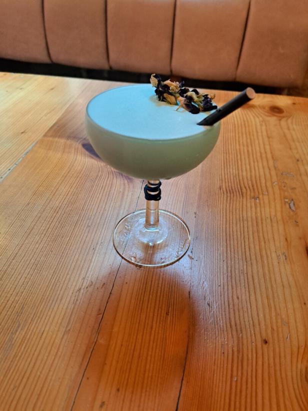 Ein hellblauer Cocktail mit Strohhalm und Blüten auf einem Holztisch.