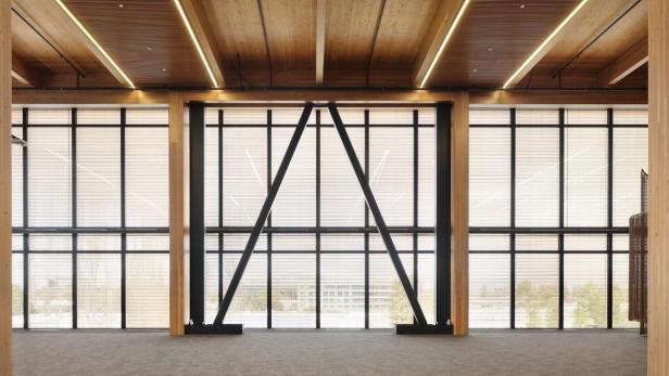 Ein Innenraum mit Holzdecke und großen Fenstern mit Jalousien, die durch Stahlträger verstärkt werden.