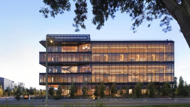 Ein modernes Bürogebäude mit Glasfassade und mehreren Etagen bei Dämmerung.