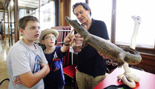 Ein Mann zeigt zwei Jungen ein Krokodil und eine Kobra auf einem Tisch.