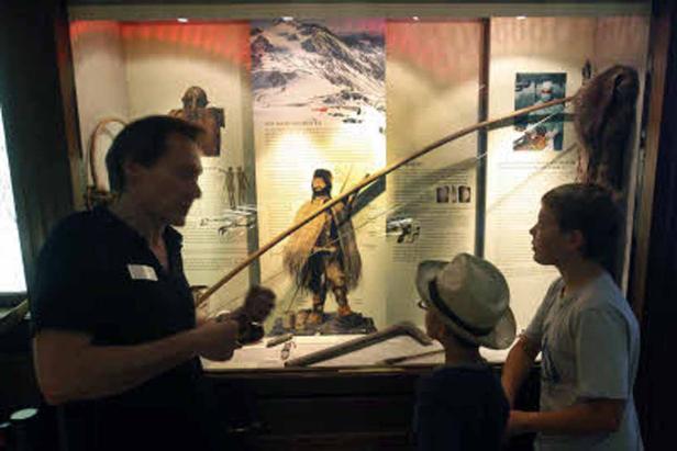 Ein Mann erklärt zwei Kindern eine Ausstellung über das Leben in den Bergen.