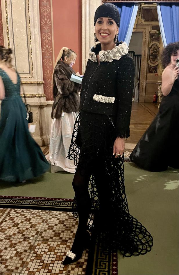 Eine Frau in einem schwarzen Outfit mit Rüschenkragen posiert in einem eleganten Raum.