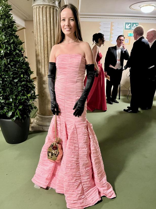 Eine Frau in einem rosa Abendkleid und schwarzen Handschuhen posiert für ein Foto.