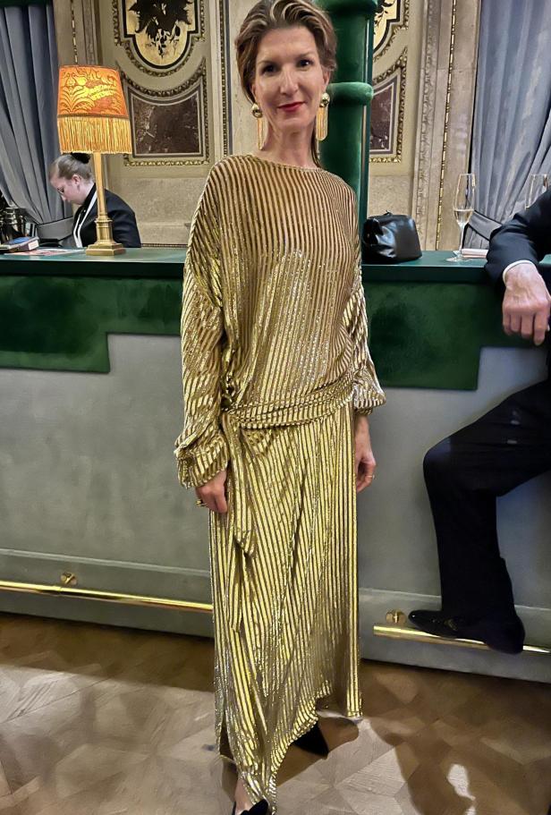 Eine Frau in einem goldenen, gestreiften Kleid steht in einem eleganten Raum.