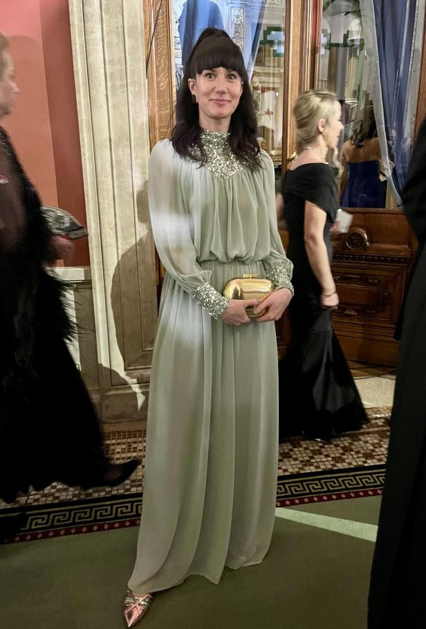 Eine Frau in einem langen, hellgrünen Kleid mit einer goldenen Clutch auf einer Veranstaltung.