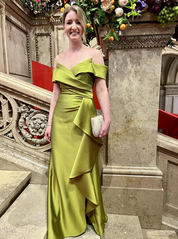 Eine Frau in einem grünen Abendkleid steht auf einer verzierten Treppe.