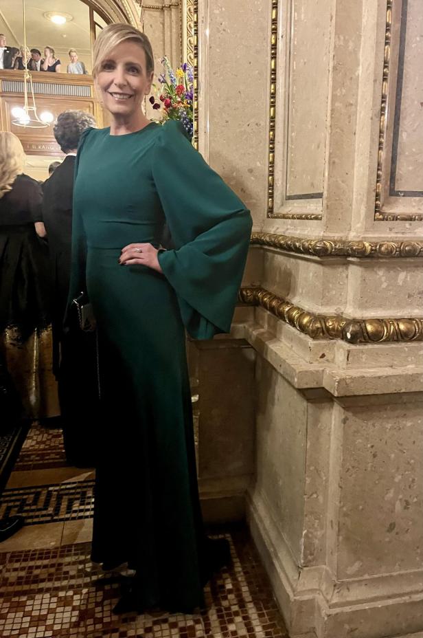 Eine Frau in einem smaragdgrünen Kleid posiert in einem eleganten Gebäude.