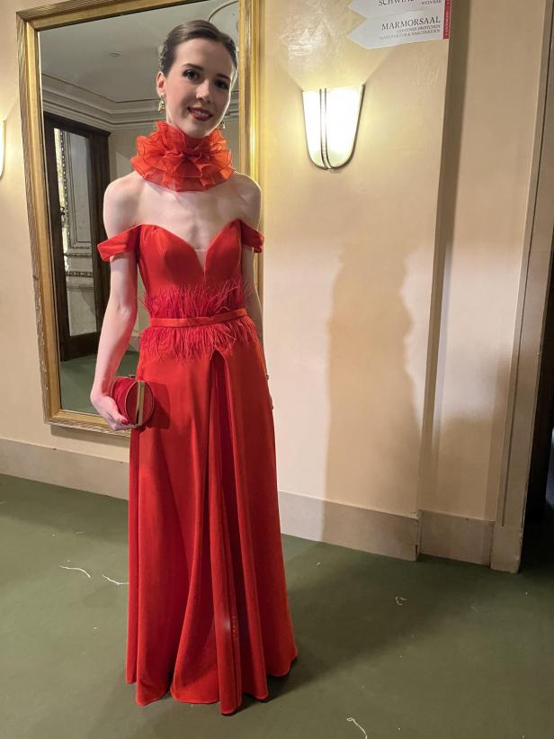 Eine Frau in einem roten Abendkleid mit Rüschenkragen und passender Handtasche.