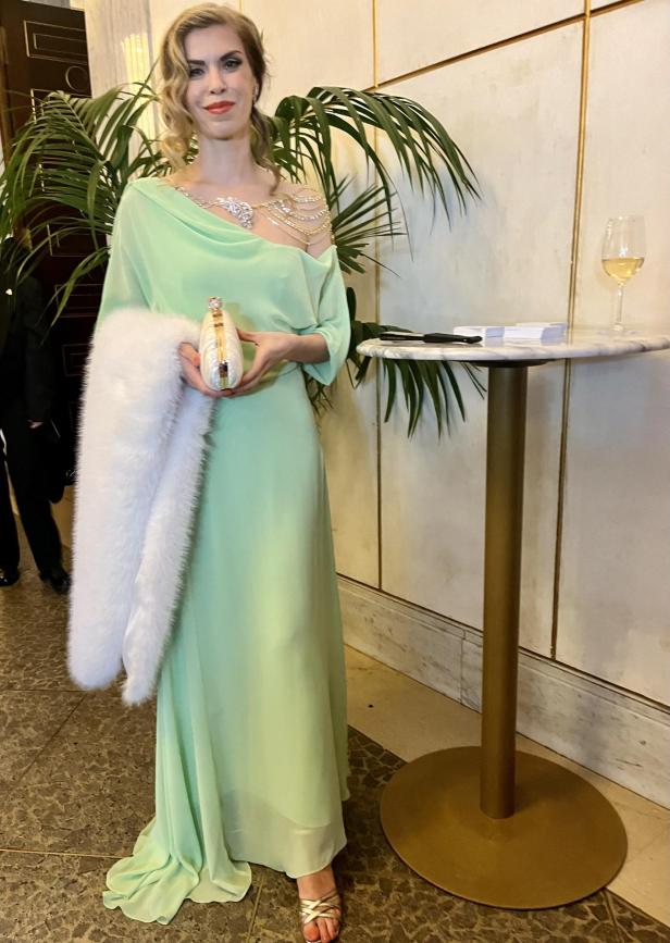 Eine Frau in einem mintgrünen Kleid mit Stola und Schmuck steht in einem Raum.