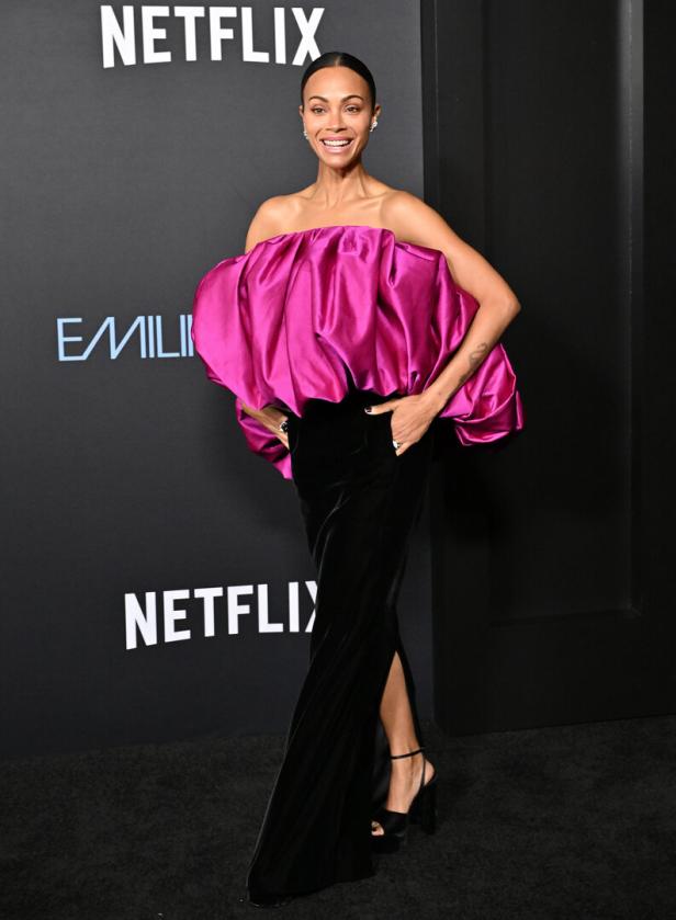 Zoe Saldaña in einem pinkfarbenen Oberteil und einem schwarzen Rock auf dem roten Teppich.