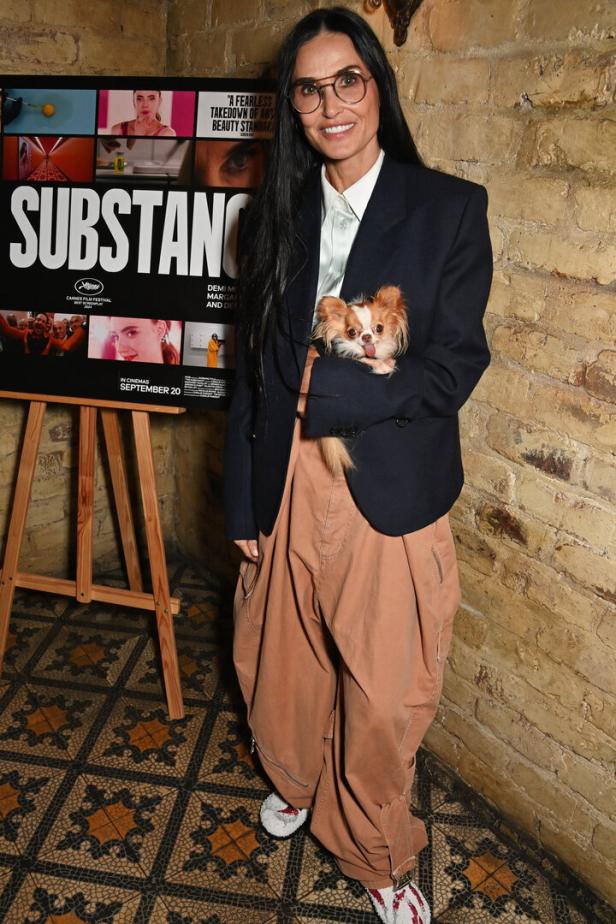Demi Moore posiert mit ihrem Chihuahua vor einem Filmplakat für „The Substance“.