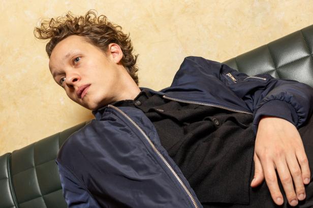 Ein Mann mit lockigem Haar liegt auf einer grünen Couch.