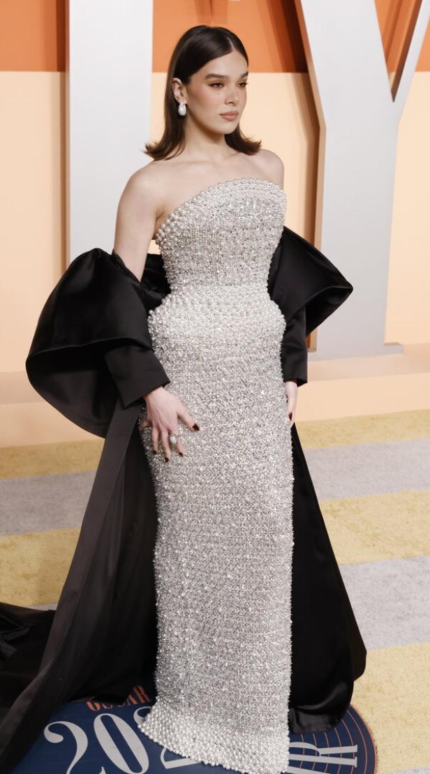 Hailee Steinfeld in einem silbernen, trägerlosen Kleid mit schwarzem Umhang.