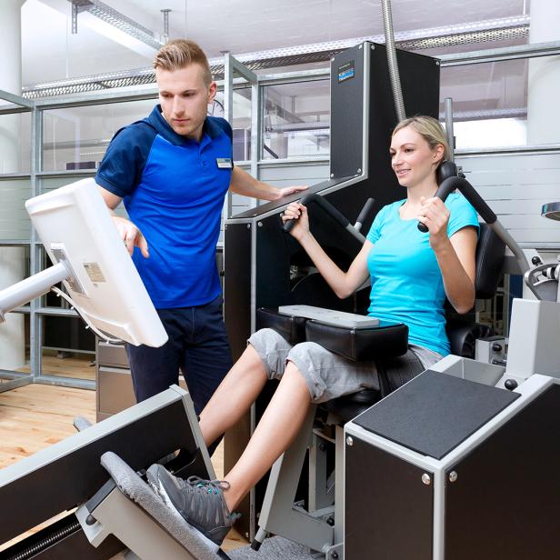 Eine Frau trainiert im Fitnessstudio, ein Mann hilft ihr. 