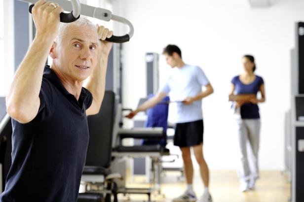 Ein älterer Mann im schwarzen T-Shirt trainiert in einem Fitnessstudio. 