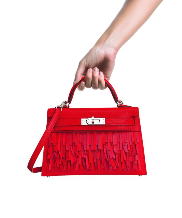 Eine Hand hält eine rote Handtasche mit Fransen.