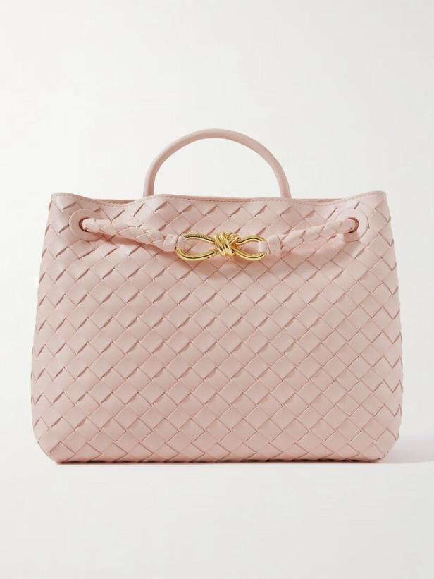 Eine hellrosa, gewebte Handtasche mit goldenem Verschluss vor einem weißen Hintergrund.