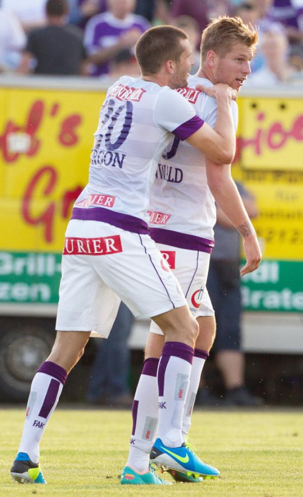 Zwei Fußballspieler in weißen Trikots umarmen sich auf dem Spielfeld.