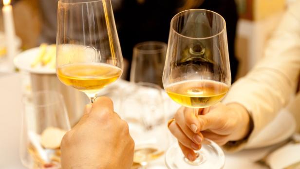 Zwei Personen stoßen mit Weißweingläsern an.