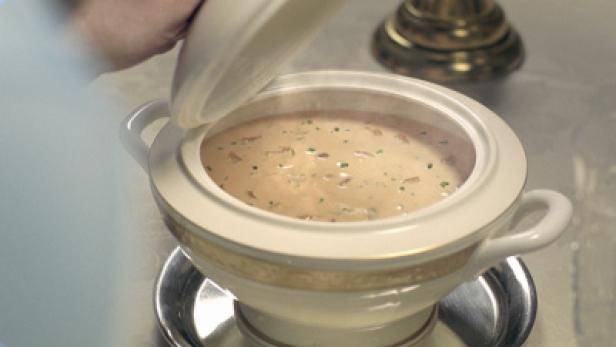 Eine dampfende Suppe wird in einer weißen Terrine mit Goldrand serviert.