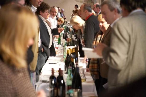 Menschen stehen an einem Tisch mit Weinflaschen und probieren Wein.