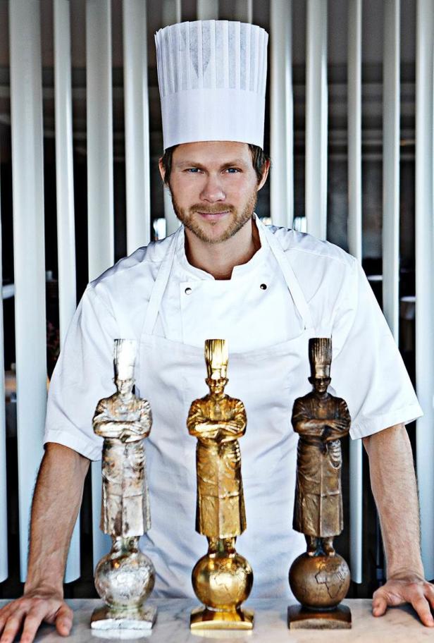 Ein Koch steht hinter drei Statuen, die Köche darstellen.