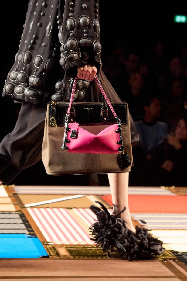 Ein Model präsentiert eine braune Louis Vuitton Tasche mit pinkfarbenem Detail und einen extravaganten Schuh auf dem Laufsteg.