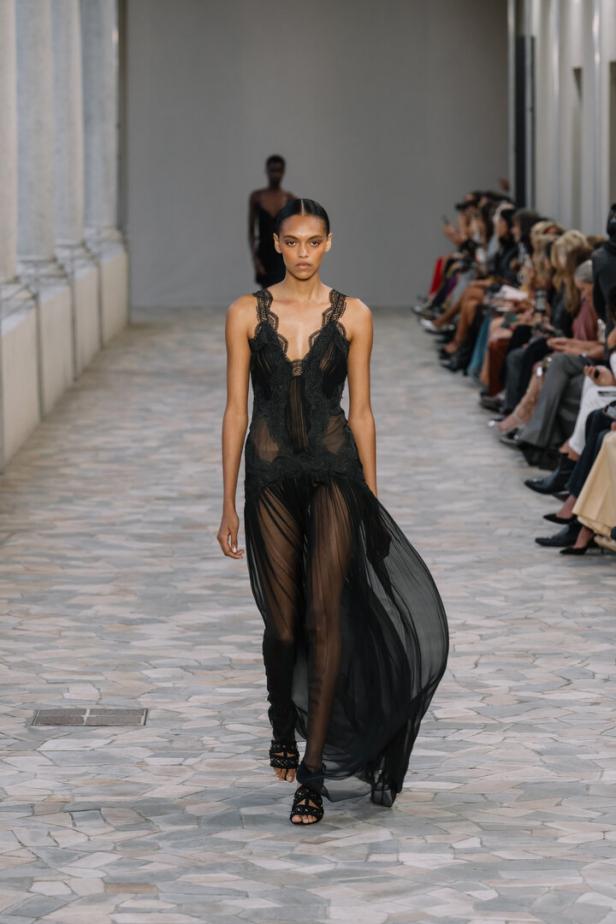 Eine Frau in einem transparenten, schwarzen Kleid auf einem Laufsteg.