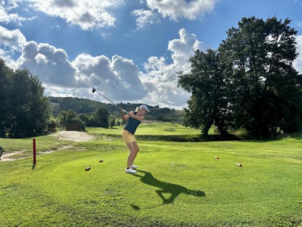 Eine Frau schwingt einen Golfschläger auf einem grünen Golfplatz.