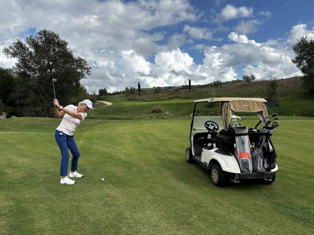 Eine Frau schwingt einen Golfschläger auf einem Golfplatz neben einem Golfwagen.