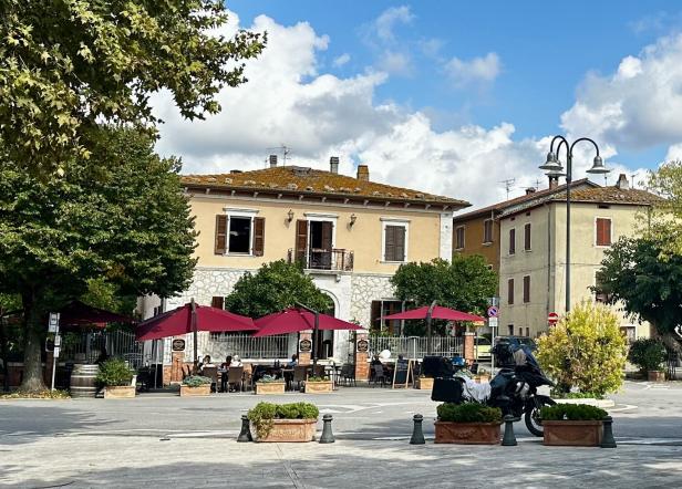 Ein Platz mit einem Restaurant mit rotem Sonnenschirm und einem geparkten Motorrad.