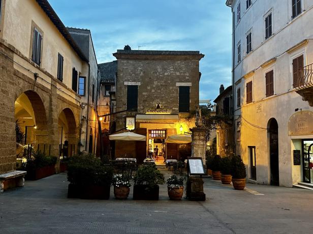 Ein Platz in einer italienischen Stadt mit einem Restaurant und einer Bar bei Dämmerung.
