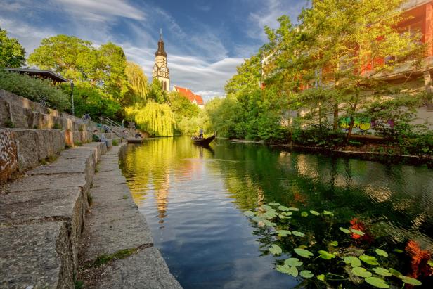 Ein Boot fährt auf einem Kanal entlang, an dessen Ufer Menschen auf Treppen sitzen.