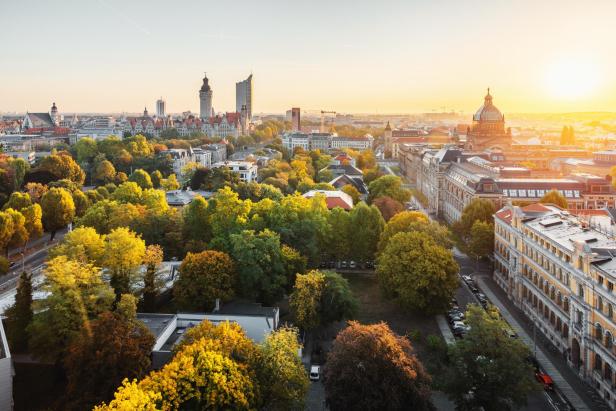 Eine Stadt von oben mit vielen grünen Bäumen, einer Altstadt im Hintergrund und einer untergehenden Sonne.