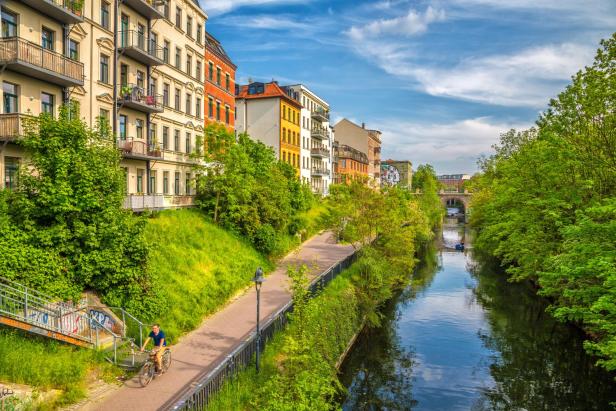 Ein Kanal, neben dem ein Fahrradweg verläuft und Wohnhäuser stehen. Es gibt viel Grün.