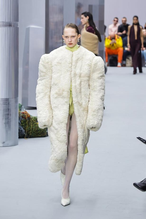 Ein Model präsentiert einen übergroßen, weißen Teddyfellmantel auf einem Laufsteg.