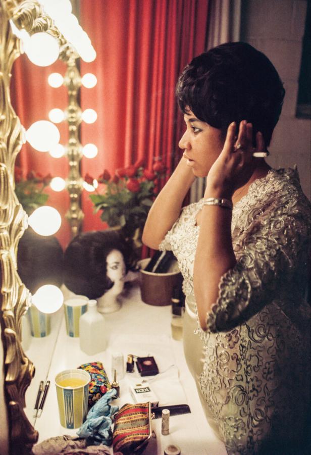 Aretha Franklin vor einem Spiegel mit Glühbirnen, während sie ihr Haar richtet.