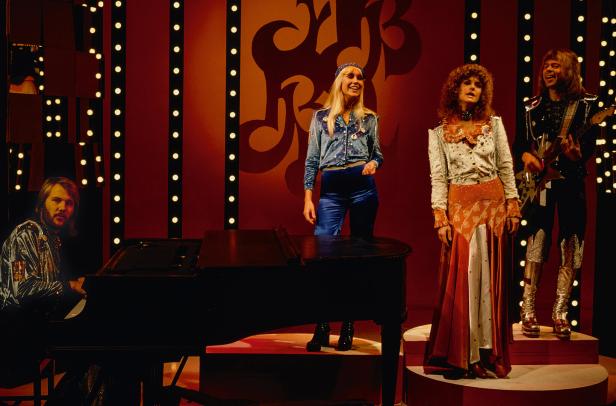 Die Band ABBA tritt auf einer Bühne vor einem roten Hintergrund auf.