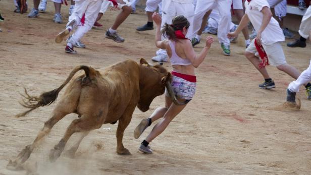 Eine Frau rennt bei einem Stierlauf vor einem Stier davon.