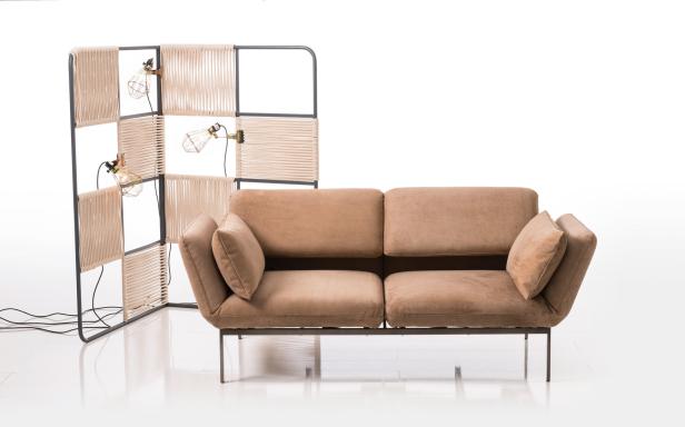 Ein beiges Sofa mit passenden Kissen steht vor einem Raumteiler mit integrierten Lampen.