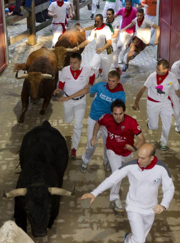 Beim Stiertreiben in Pamplona rennen Menschen vor einer Gruppe Stiere davon.