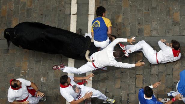 Beim Stiertreiben in Pamplona rennen Menschen vor einem schwarzen Stier davon.