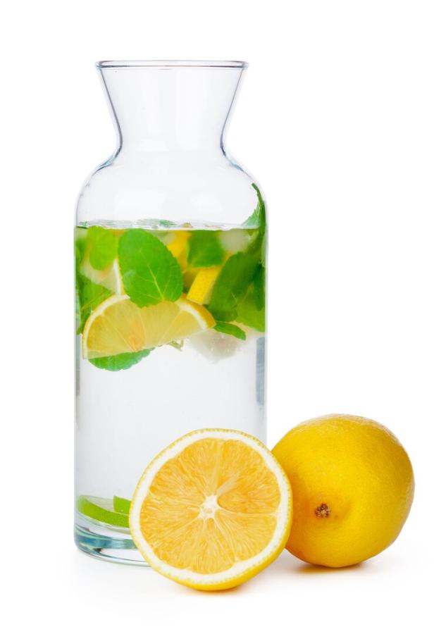 Ein Glas Wasser mit Zitrone und Minze steht neben zwei Zitronen.