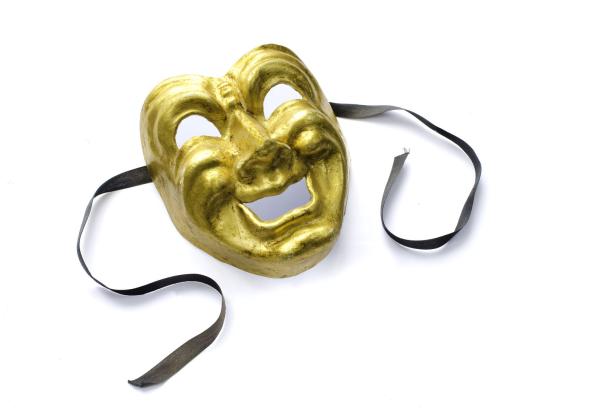 Eine goldene Theatermaske mit einem schwarzen Band liegt auf einem weißen Hintergrund.